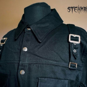 May include: A black long-sleeved shirt with a button-down collar and silver buckles on the shoulders. The shirt has a pocket on the left chest and a seam across the chest.
