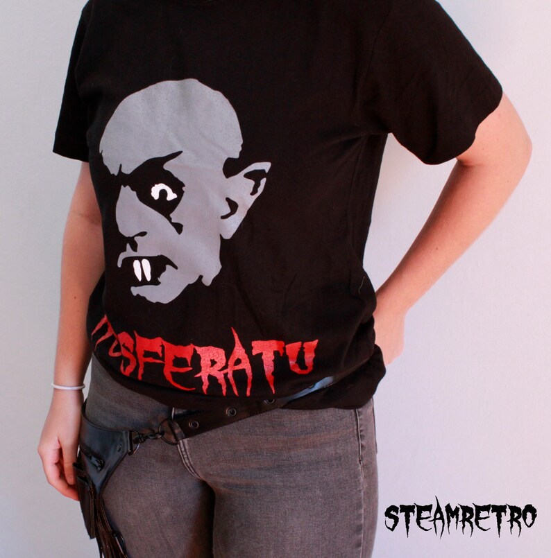 May include: Black t-shirt featuring a white graphic of a vampire's face and the word "Nosferatu" in red.