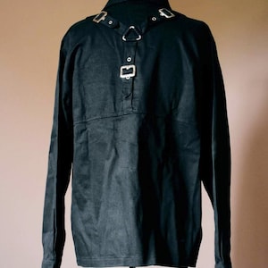 May include: A black long-sleeved shirt with a collar and a silver buckle detail on the front. The shirt is on a mannequin.