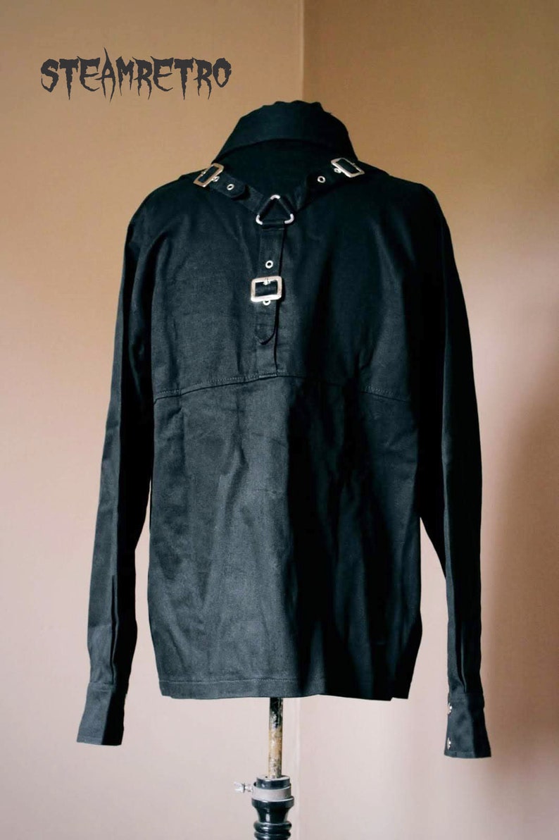 May include: A black long-sleeved shirt with a collar and a silver buckle detail on the front. The shirt is on a mannequin.