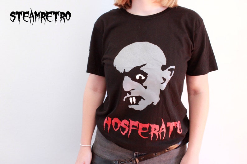 May include: A black t-shirt featuring a white and grey graphic of Count Orlok from the film Nosferatu. The text "NOSFERATU" is printed in red below the graphic.
