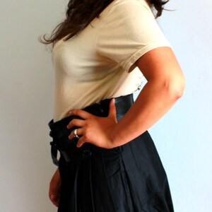 May include: A woman wearing a white t-shirt and a black pleated skirt. She is standing in front of a white wall. The text "STEAMRETRO" is visible in the top left corner of the image.