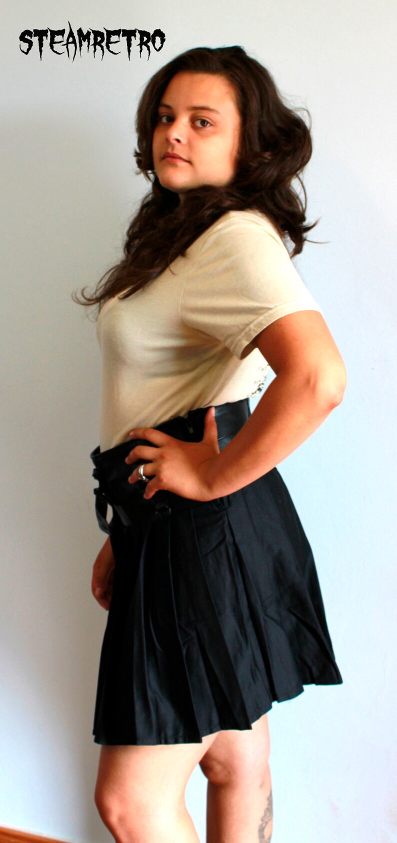 May include: A woman wearing a white t-shirt and a black pleated skirt. She is standing in front of a white wall. The text "STEAMRETRO" is visible in the top left corner of the image.