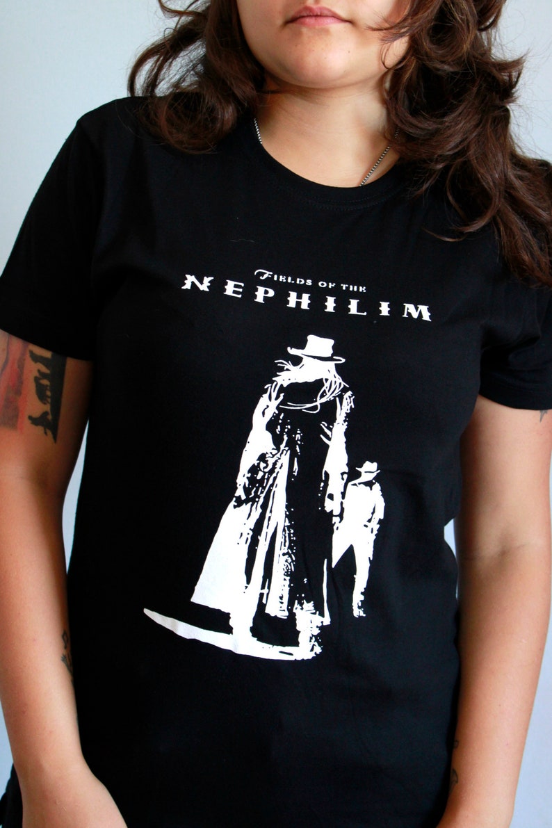 May include: Black t-shirt with a white graphic of a person in a long coat and hat. The text "Fields of the Nephilim" is printed on the shirt.