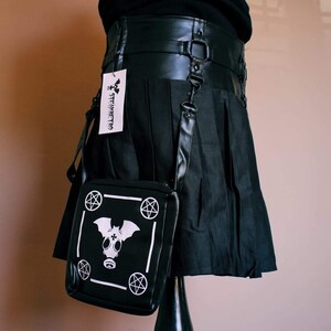 May include: Black pleated skirt with a black leather belt and a black and white crossbody bag with a gas mask and pentagram design. The bag has a white tag with the text "STEAMPUNK" on it.