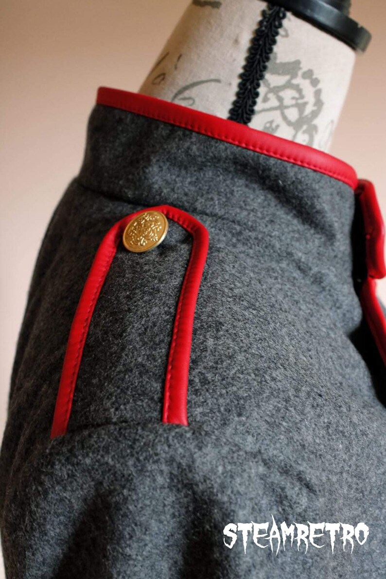 May include: Close-up of a gray wool jacket with red leather trim and a gold button. The jacket has a classic military style.