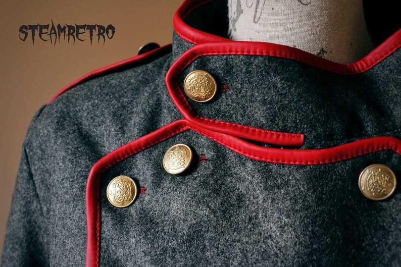 May include: Close-up of a gray wool jacket with a red leather trim and gold buttons. The jacket has a double-breasted closure and a high collar.