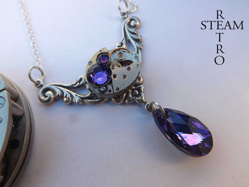 May include: A silver necklace with a steampunk-style pendant featuring a watch face with purple rhinestones and a dangling purple crystal.
