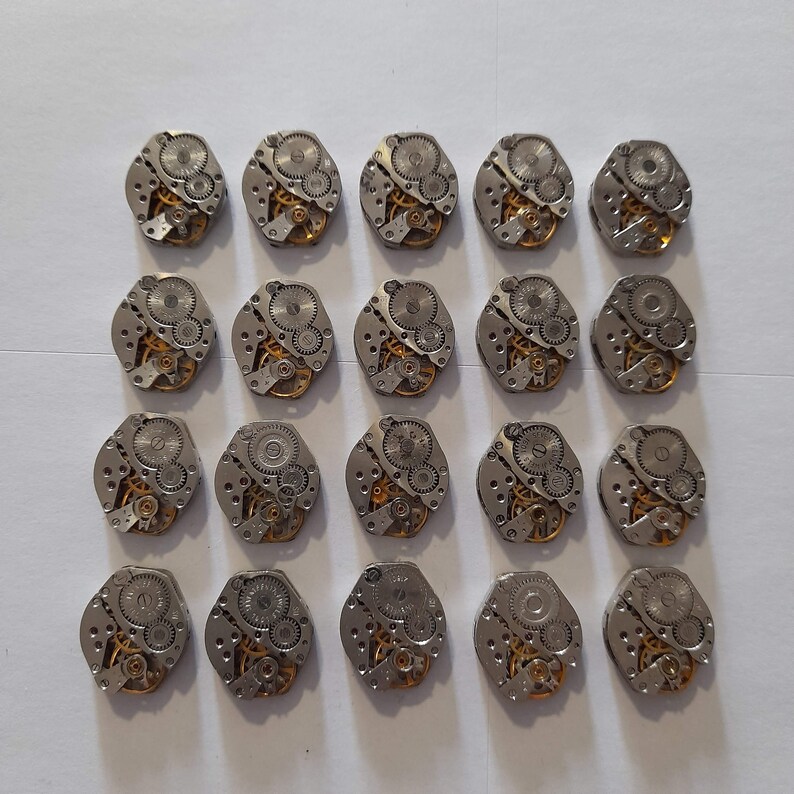 May include: Twenty-four silver-toned watch movements with intricate gold gears and a circular shape.