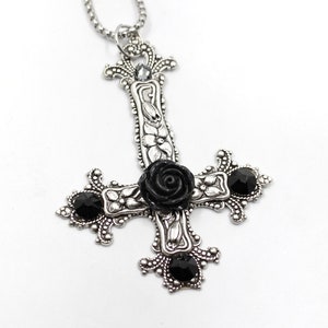 Puede incluir: Un collar con un colgante de plata en forma de cruz invertida adornado con una rosa negra y piedras preciosas negras.