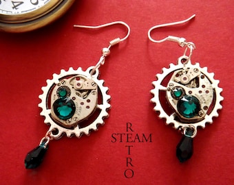 May include: A pair of silver steampunk earrings with green crystal accents. Each earring features a circular gear with a watch face and a dangling green crystal drop.