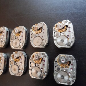 Peut inclure: Dix mouvements de montres argent&eacute;s avec des engrenages complexes et une tige de remontage dor&eacute;e. Les mouvements sont dispos&eacute;s en deux rang&eacute;es de cinq.