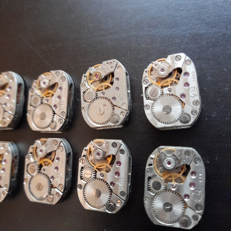 Peut inclure: Dix mouvements de montres argent&eacute;s avec des engrenages complexes et une tige de remontage dor&eacute;e. Les mouvements sont dispos&eacute;s en deux rang&eacute;es de cinq.