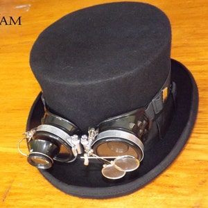 Peut inclure: Un chapeau haut de forme noir avec un bandeau noir et une paire de lunettes steampunk argent&eacute;es et noires fix&eacute;es &agrave; l'avant.