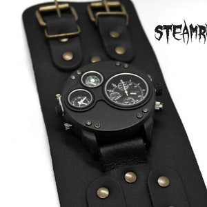 Puede incluir: Un reloj de pulsera de cuero negro con una esfera grande y redonda y varios sub-diales. El reloj tiene una correa negra con múltiples correas y hebillas.
