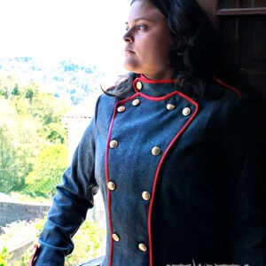 May include: A woman wearing a gray jacket with red trim and gold buttons. The jacket has a double-breasted closure and a stand-up collar.