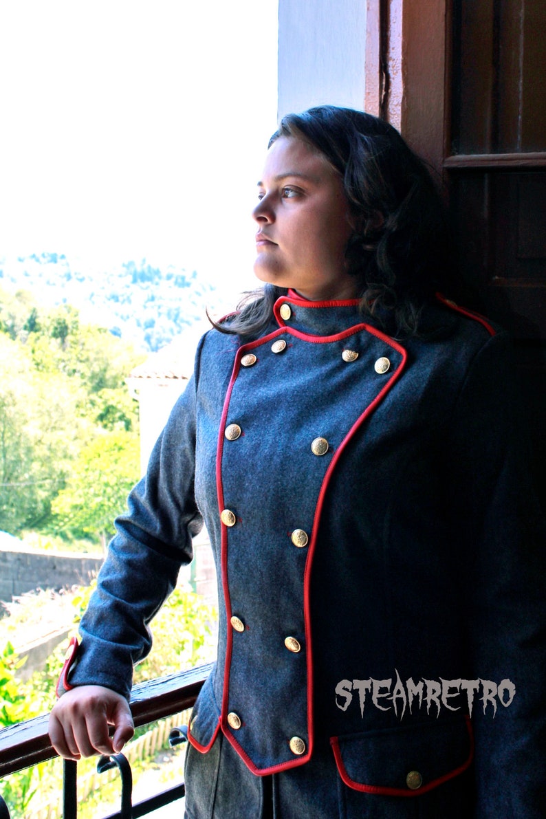 May include: A woman wearing a gray jacket with red trim and gold buttons. The jacket has a double-breasted closure and a stand-up collar.