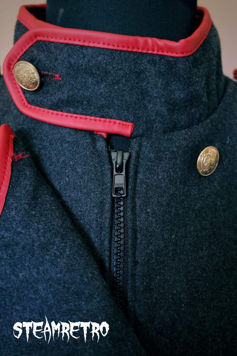 May include: A dark gray jacket with a red leather trim around the collar and a black zipper. The jacket has two gold buttons on the front.