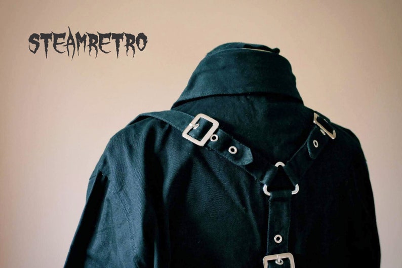May include: A black shirt with a dark green hue, featuring a silver buckle and straps on the back. The straps are in a Y-shape and have multiple silver buckles and rings.