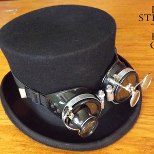 Peut inclure: Un chapeau haut de forme noir avec des lunettes de style steampunk noires et argent&eacute;es fix&eacute;es au bord. Les lunettes ont une loupe sur le c&ocirc;t&eacute;.
