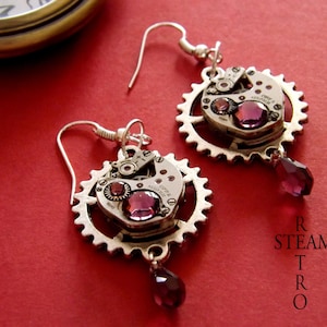 May include: A pair of silver earrings with a steampunk design. Each earring features a circular gear with a watch face and a purple crystal dangling from the bottom.