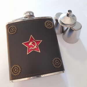 May include: A black leather flask with a silver metal top and a red star with a hammer and sickle design. The flask has several decorative gears around the edges.