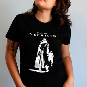 May include: A person wearing a black t-shirt with a white graphic of a figure in a top hat and the text "Fields of the Nephilim". The person is wearing black pants with silver grommets.
