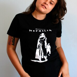 May include: A person wearing a black t-shirt with a white graphic of a figure in a long coat and hat. The text "Fields of the Nephilim" is printed on the shirt.