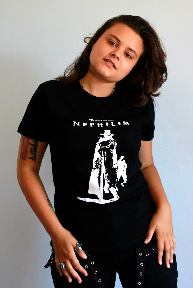 May include: A person wearing a black t-shirt with a white graphic of a figure in a long coat and hat. The text "Fields of the Nephilim" is printed on the shirt.