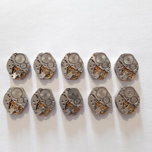 May include: Ten silver watch movements with intricate gold gears and a circular shape.