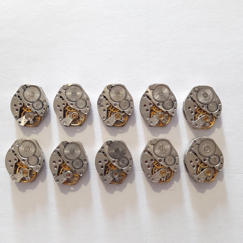 May include: Ten silver watch movements with intricate gold gears and a circular shape.