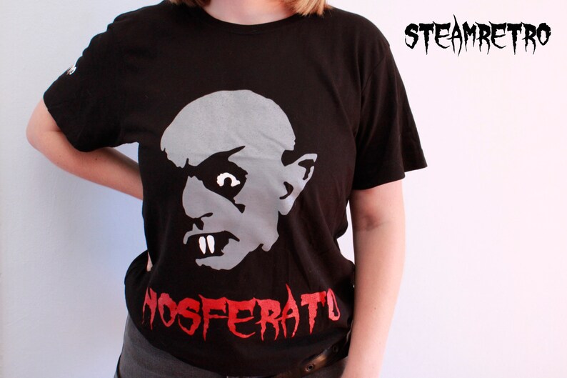 May include: Black t-shirt featuring a white graphic of a vampire's face and the text "NOSFERATU" in red.