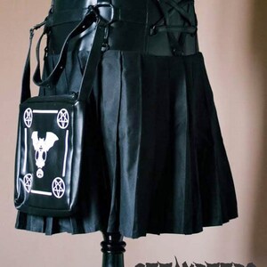 May include: Black pleated skirt with a black leather belt and a black bag with a white bat and pentagram design. The bag is attached to the belt with a strap.