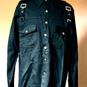 May include: A black long-sleeved shirt with a button-up front and two chest pockets. The shirt has silver buckles and straps on the shoulders.