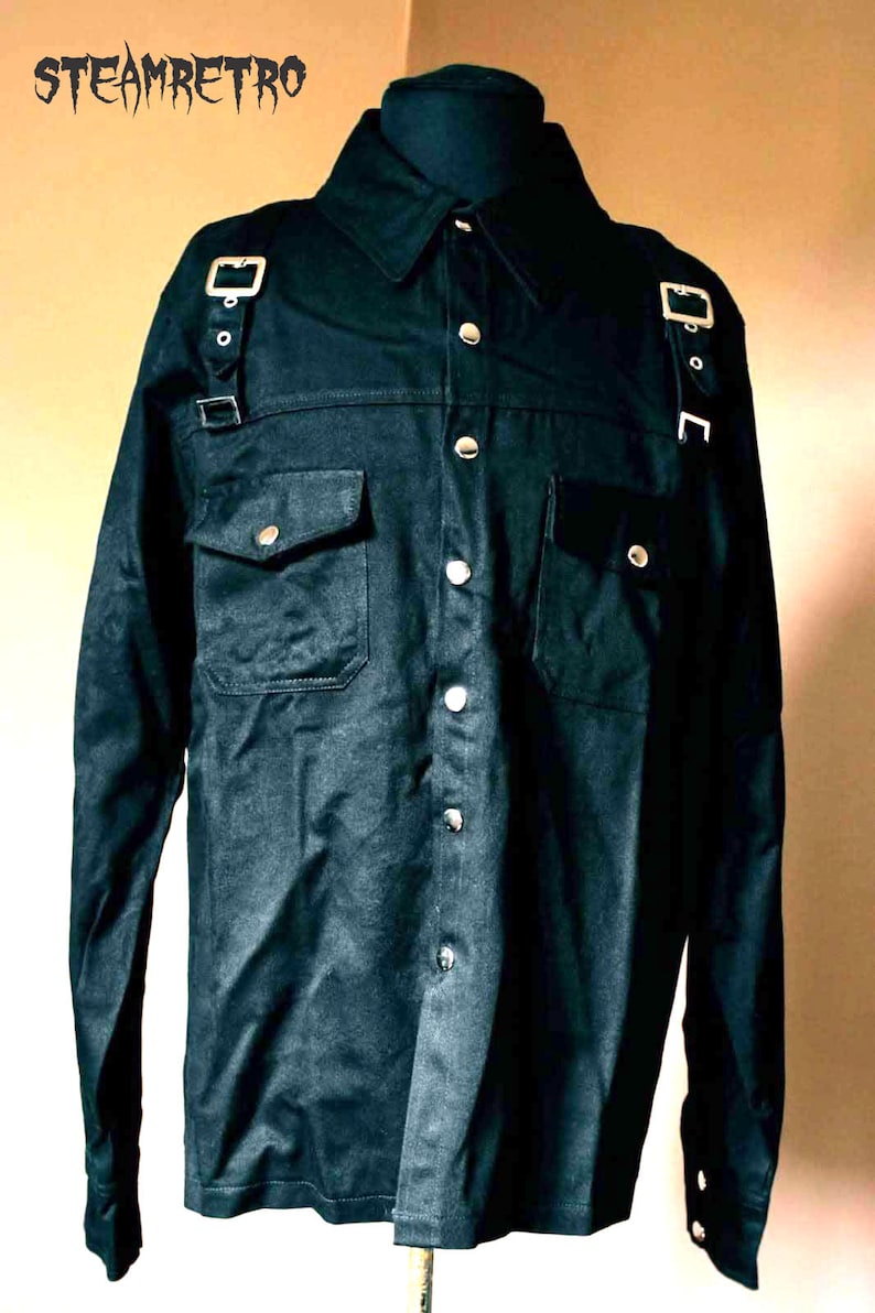 May include: A black long-sleeved shirt with a button-up front and two chest pockets. The shirt has silver buckles and straps on the shoulders.