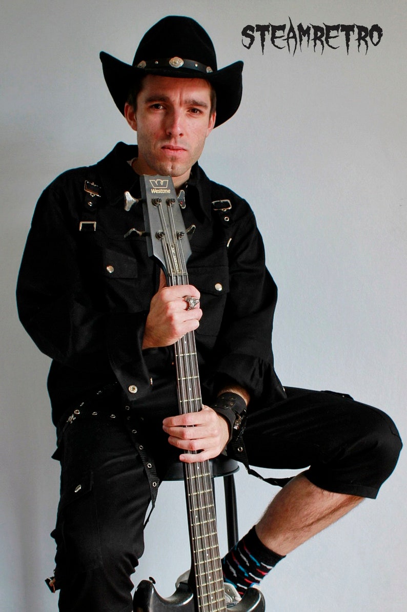 May include: A person wearing a black cowboy hat and a black shirt with a black bass guitar. The guitar has a black body and a silver headstock. The person is sitting on a stool and has a black belt with silver buckles. The text "STEAMRETRO" is in the upper right corner of the image.