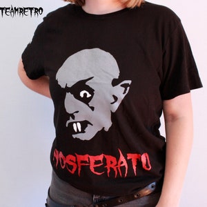 May include: Black t-shirt featuring a white graphic of a vampire's face and the red text "NOSFERATU".