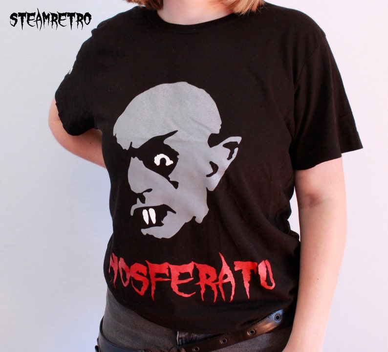 May include: Black t-shirt featuring a white graphic of a vampire's face and the red text "NOSFERATU".