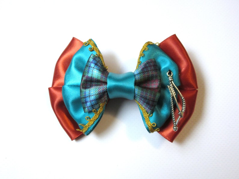 May include: A turquoise and orange bow with a plaid center and a silver arrow charm.