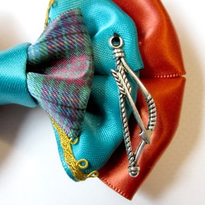 May include: A turquoise, orange, and plaid bow with a silver arrow charm.
