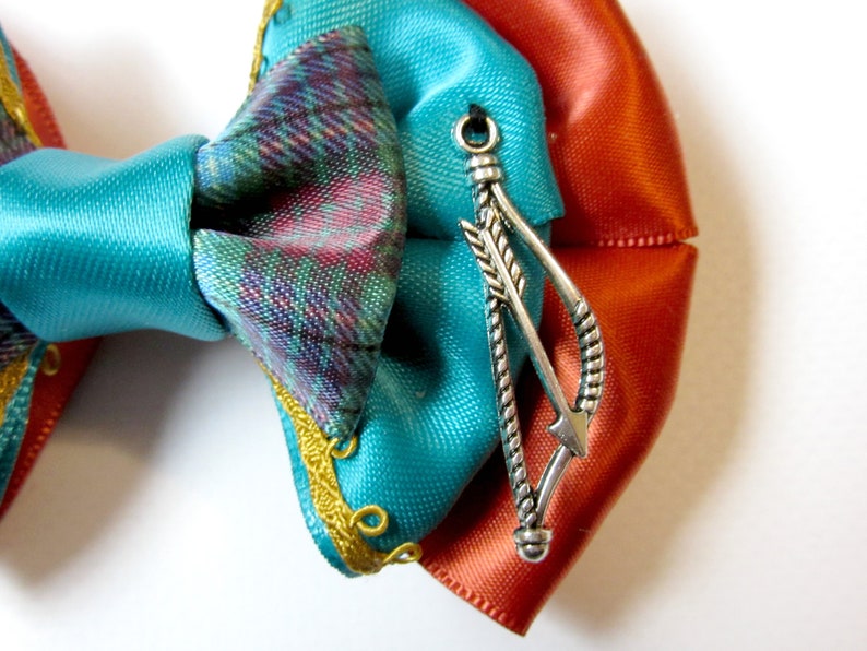 May include: A turquoise, orange, and plaid bow with a silver arrow charm.
