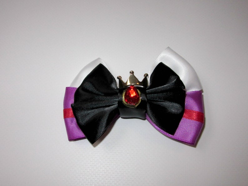 May include: A black satin bow with a purple and white ribbon, accented with a silver crown and a red gem.