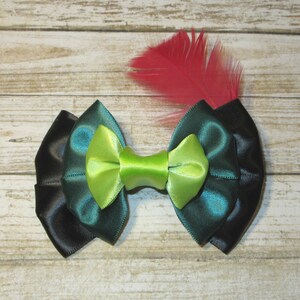 Puede incluir: Un lazo de sat&eacute;n negro, verde azulado y verde lima con un acento de pluma roja. El lazo est&aacute; atado en un estilo cl&aacute;sico y ser&iacute;a una gran adici&oacute;n a cualquier colecci&oacute;n de accesorios para el cabello.