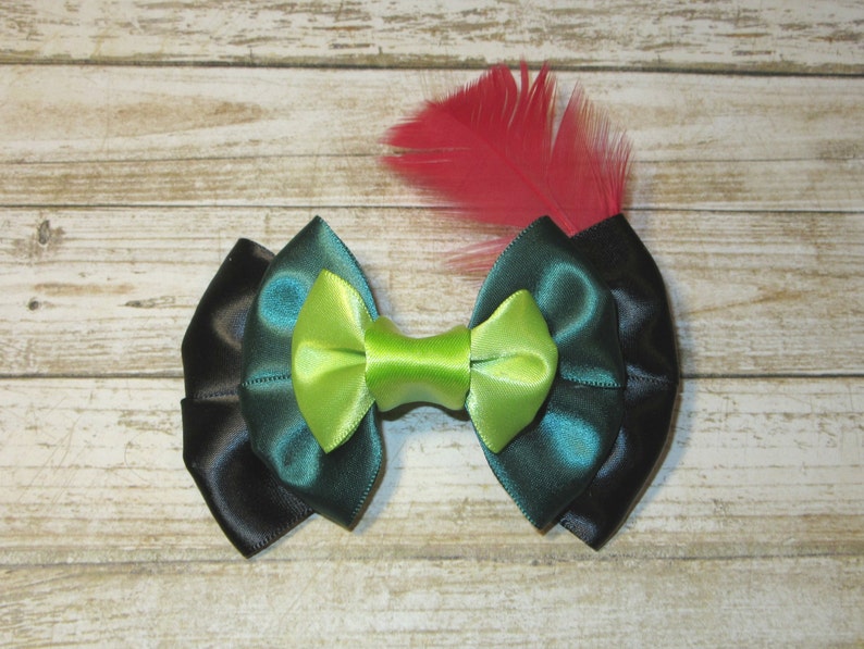 Puede incluir: Un lazo de sat&eacute;n negro, verde azulado y verde lima con un acento de pluma roja. El lazo est&aacute; atado en un estilo cl&aacute;sico y ser&iacute;a una gran adici&oacute;n a cualquier colecci&oacute;n de accesorios para el cabello.