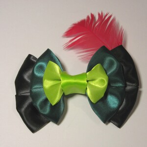 Puede incluir: Un lazo verde y negro con un centro verde lima y una sola pluma rosa.