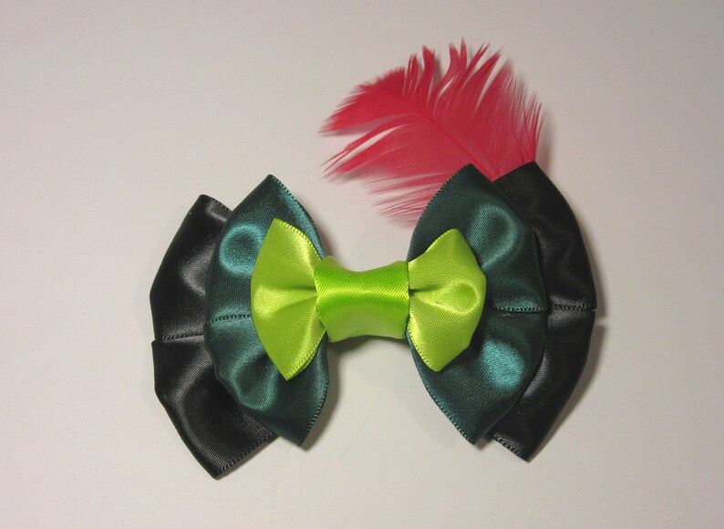 Puede incluir: Un lazo verde y negro con un centro verde lima y una sola pluma rosa.