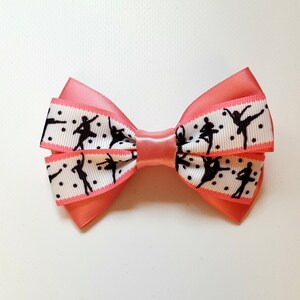 Puede incluir: Un lazo rosa con una cinta blanca con una silueta negra de bailarines y lunares blancos.