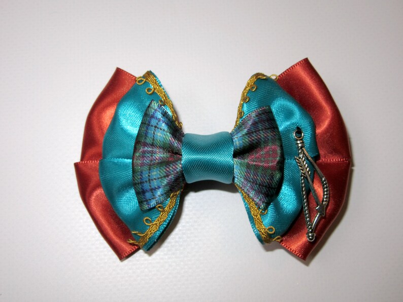 May include: A teal blue bow with a plaid pattern and gold trim. The bow has a red and orange base and a silver feather charm.