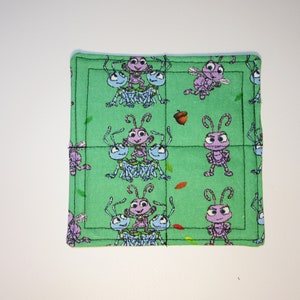 Może przedstawiać: Zielona podkładka pod kubek wykonana z tkaniny z powtarzającym się wzorem fioletowych i niebieskich kresk&oacute;wkowych mr&oacute;wek. Mr&oacute;wki znajdują się na zielonym tle z brązowymi liśćmi i żołędziami.