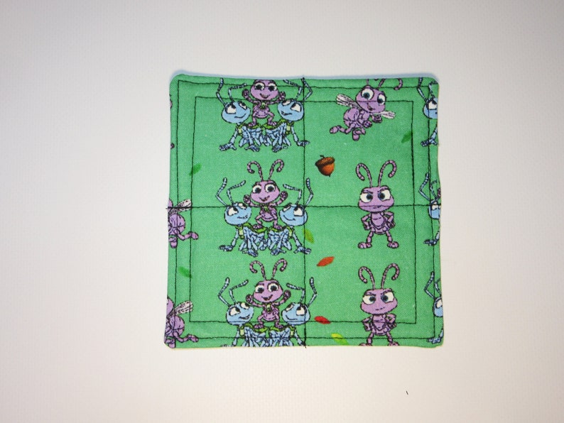 Może przedstawiać: Zielona podkładka pod kubek wykonana z tkaniny z powtarzającym się wzorem fioletowych i niebieskich kresk&oacute;wkowych mr&oacute;wek. Mr&oacute;wki znajdują się na zielonym tle z brązowymi liśćmi i żołędziami.